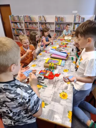 Dzieci siedzą przy stoliku i malują farbami swoje dłonie.