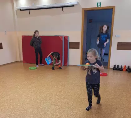 Dziewczynka niesie na książce piłeczkę.