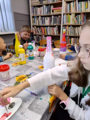 Dzieci siedzą przy stole i malują farbkami prezent dla mamy