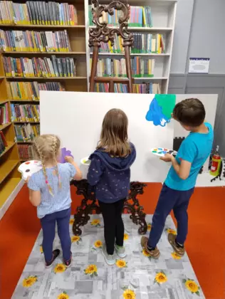 Dzieci na dużej kartce malują farbami obraz.
