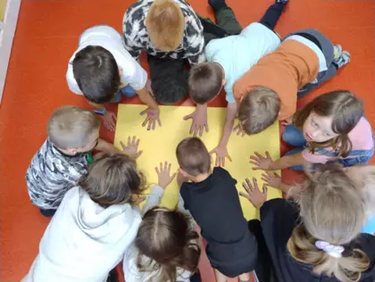 Dzieci na dużej kartce papieru odbijają swoje ręce w farbie.