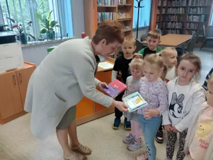 Pani bibliotekarka w trakcie przyjmowania prezentu z rąk przedszkolaków.