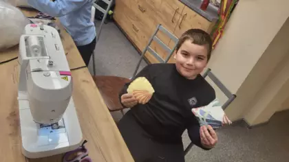 Chłopczyk siedzi pezy stole obok maszyny ze swoją uszytą pracą.