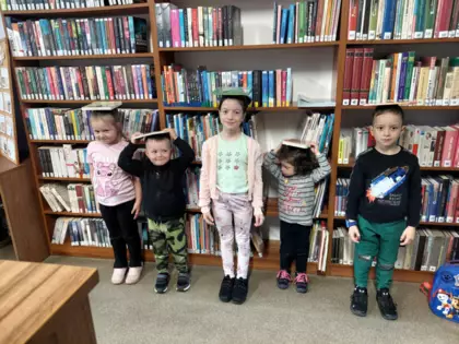 Dzieci stoją z książkami na głowie.