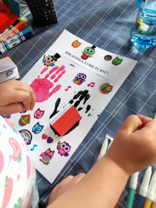 Gotowy mini plakat. Odbita rączka, a na niej przyklejona książeczka napisana przez dzieci.