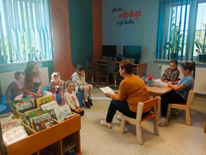 Dzieci słuchają bajki czytanej przez panią bibliotekarkę.