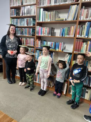 Dzieci stoja z książkami na głowie.