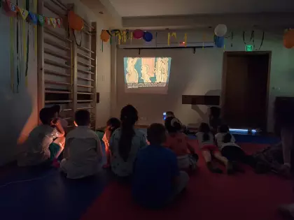 Dzieci siedzą i oglądają bajki wyświetlane na projektorze.