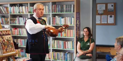 Pan Marek Szołtysek pokazuje instrument podobny do mandoliny. Za nim, na sztaludze plakat ukazujący trubadurów.