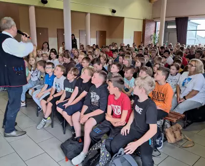 Na korytarzu szkolnym siedzą na ławach uczniowie i słuchają Pana Marka Szołtyska.