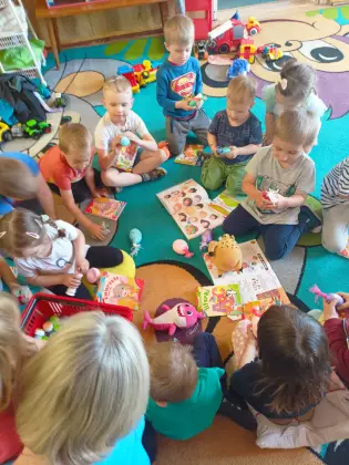 Dzieci siedzą na dywanie i oglądają książeczki.