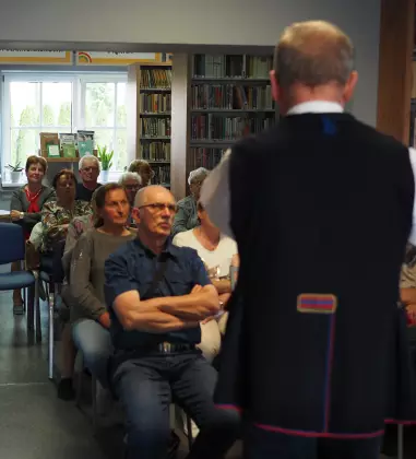 W bibliotece Pan Marek Szołtysek mówi do ludzi siedzących na krzesłach.
