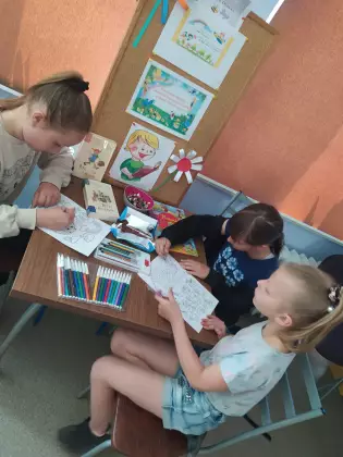 Dzieci siedzą przy stoliku i kolorują obrazki.