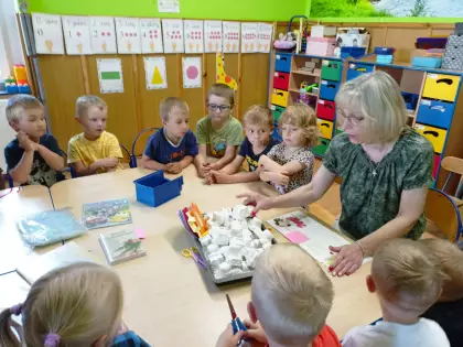 Przedszkolaki siedzą przy wspólnym stole i słuchają czytanej bajki.