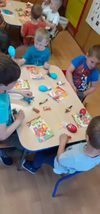 Dzieci siedzą przy stolikach w przedszkolu i kolorują obrazki.