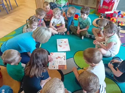 Pani bibliotekarka czyta dzieciom książki na dywanie w przedszkolu.