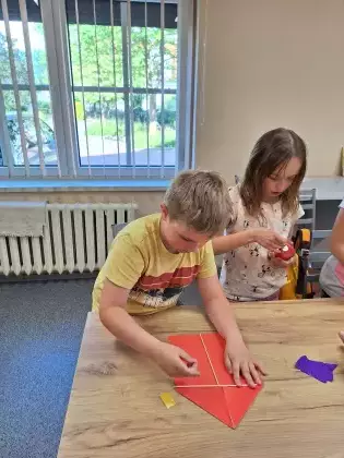 Chłopak na zajęciach plastycznych skleja latawiec.