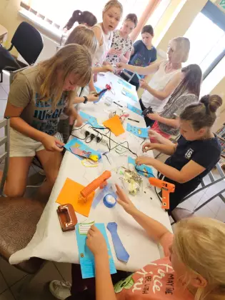 Uczestnicy zajęć siedzą przy stole i z kolorowego papieru wykonują laurki na Dzień Ojca.