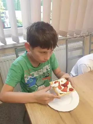 Chłopczyk je gofra z bitą śmietaną i truskawkami.