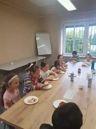 Uczestnicy zajęć siedzą przy stole i jedzą gofry z owocami.