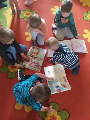 Dzieci oglądają książki na dywanie.