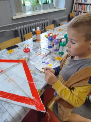 Dzieci malują farbami latawce.