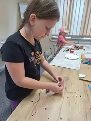 Dziewczynka nawija na sznurek korale dla mamy.