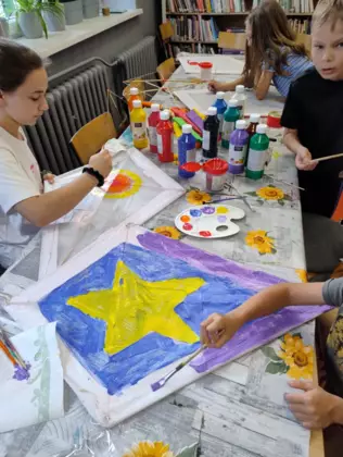 Dzieci malują farbami latawce.