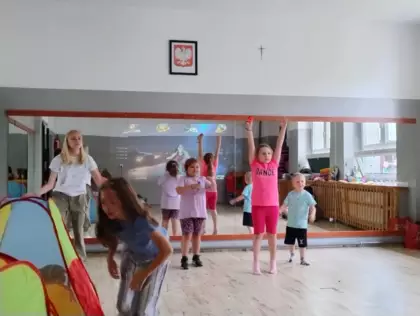 Dzieci na sali sportowej tańczą w rytm muzyki.