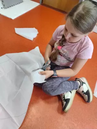 Dziewczynka wycina z materiału latawiec.