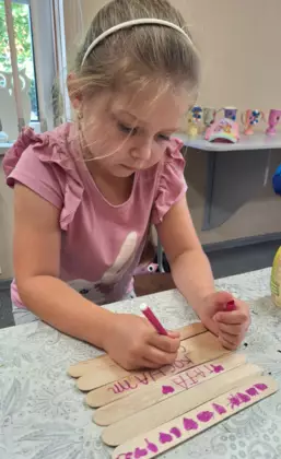 Dziewczynka mazakiem maluje obrazek dla taty.