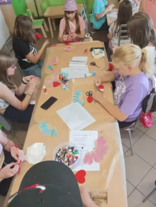 Dzieci siedzą przy stole i wyklejają serduszka dla taty.