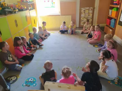 Dzieci siedzą na dywanie i słuchają opowiadania.