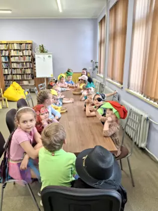 Dzieci siedzą przy stolikach w bibliotece. Mają na sobie kolorowe przebrania bajkowo-literackie