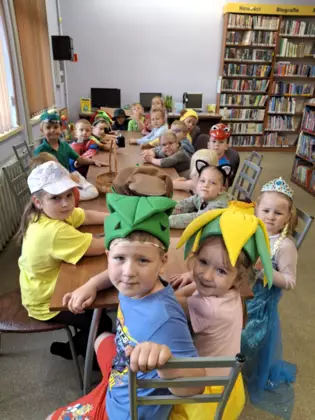 Dzieci siedzą przy stolikach w bibliotece. Mają na sobie kolorowe przebrania bajkowo-literackie.