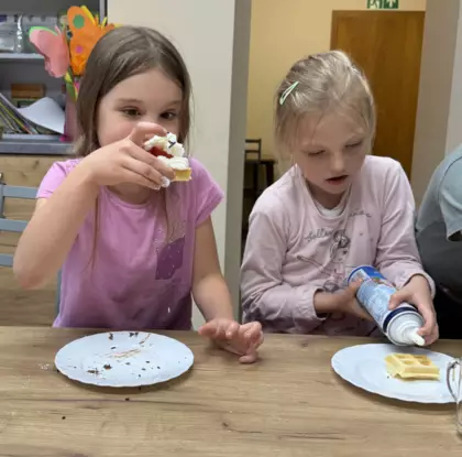 Dzieci jedzą gofry z bitą śmietaną i owocami