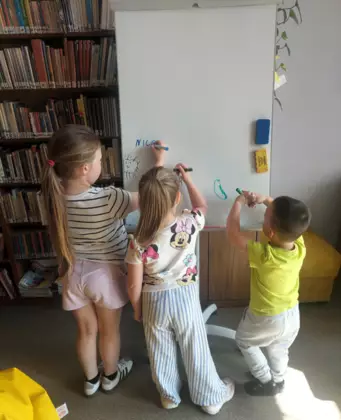 Dzieci rysują markerami na tablicy duży wiatrak.