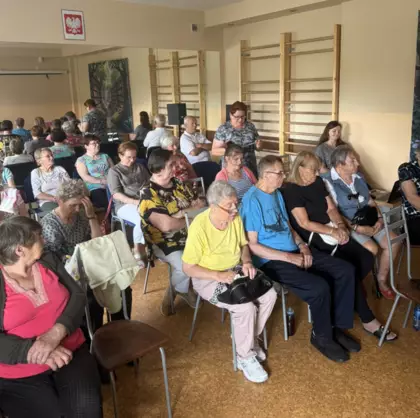 Grupa seniorów siedzi na sali. jedna z uczestniczek czyta wiersz.
