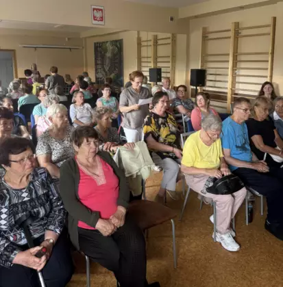 Grupa seniorów siedzi na sali. jedna z uczestniczek czyta wiersz.