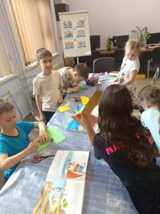 Dzieci siedzą przy stole i wykonują prace plastyczne.