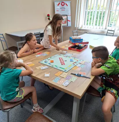Dzieci siedzą przy stole i grają w grę Monopoly.