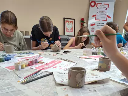 Uczestnicy warsztatów malują zrobione kubki farbą ceramiczną.