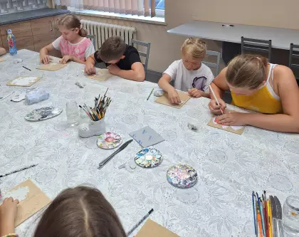 Dzieci siedzą przy stole i wyklejają masą plastyczną postać orła.