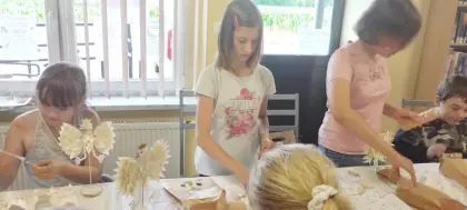 Uczestniczki warsztatów wyklejają wiórkami osikowymi statuetkę Orła Białego.