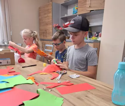 Dzieci siedzą przy stole i wycinają z papieru kolorowe rybki.