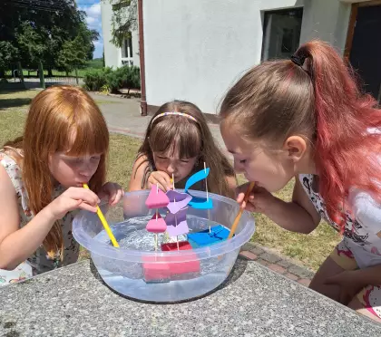 Dziewczynki puszczają na wodę statki zrobione z gąbki do mycia naczyń.