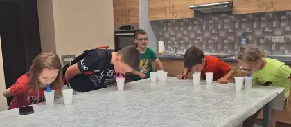 Dzieci dmuchają baloniki w kubeczkach i składają je razem.