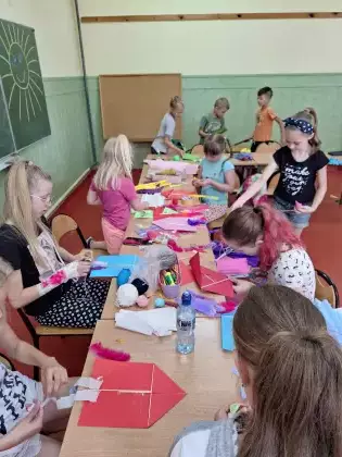 Uczestnicy zajęć sklejają latawce z kolorowego papieru.