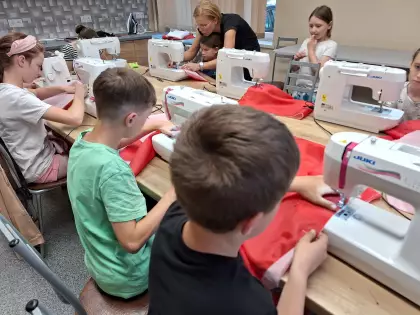 Dzieci szyją flagę Polski na maszynie.