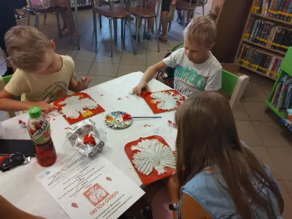 Uczestnicy spotkania malują farbami godło Polski.